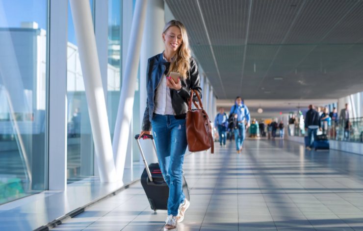 donna sorridente in aeroporto con la valigia e il cellulare in mano